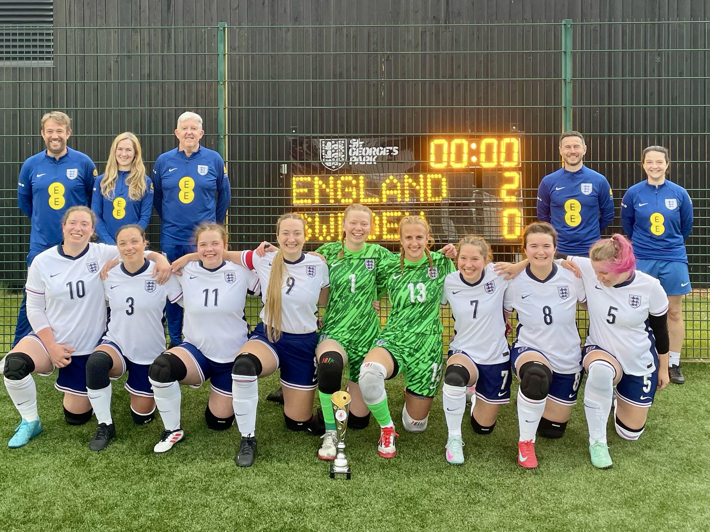 the full squad of players and coaches standing in front of the scoreboard which shows the final result