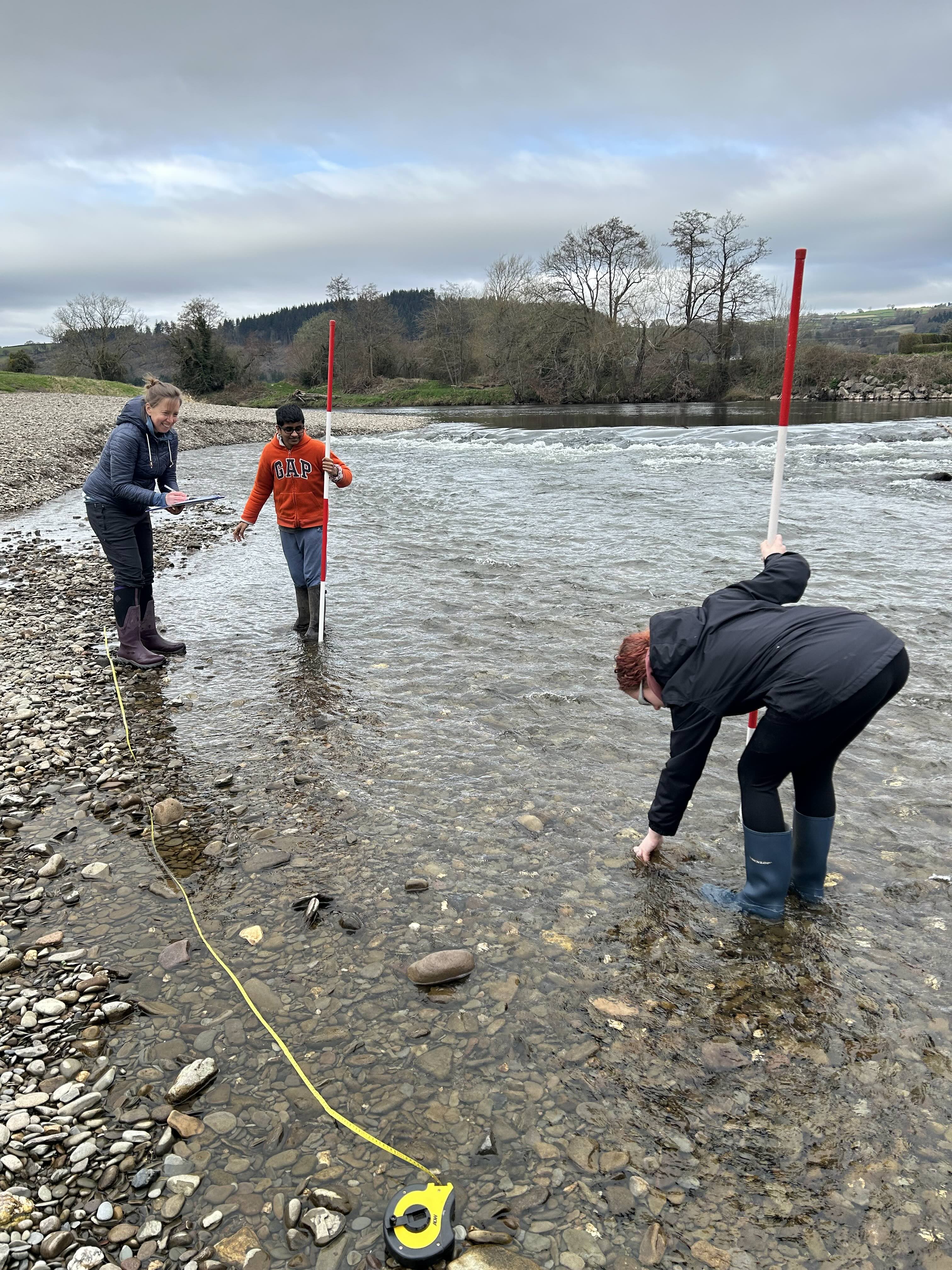 3 people standing in the shallow edge of the the River Wye. They are using various instruments to undertake their study