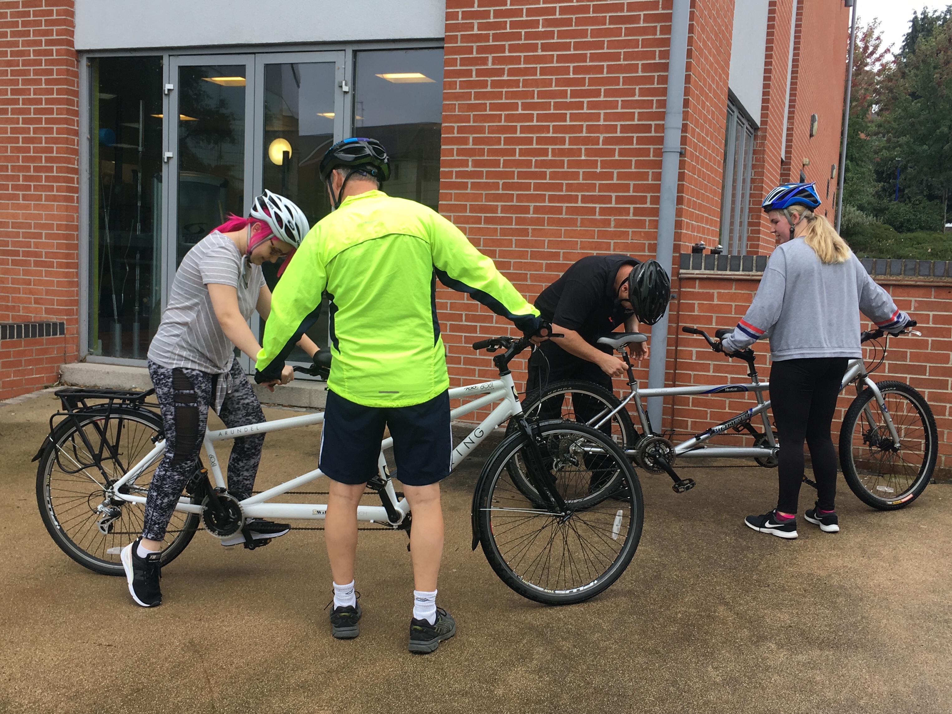 two male tandem pilots adjust the bike seats to suit their female riders