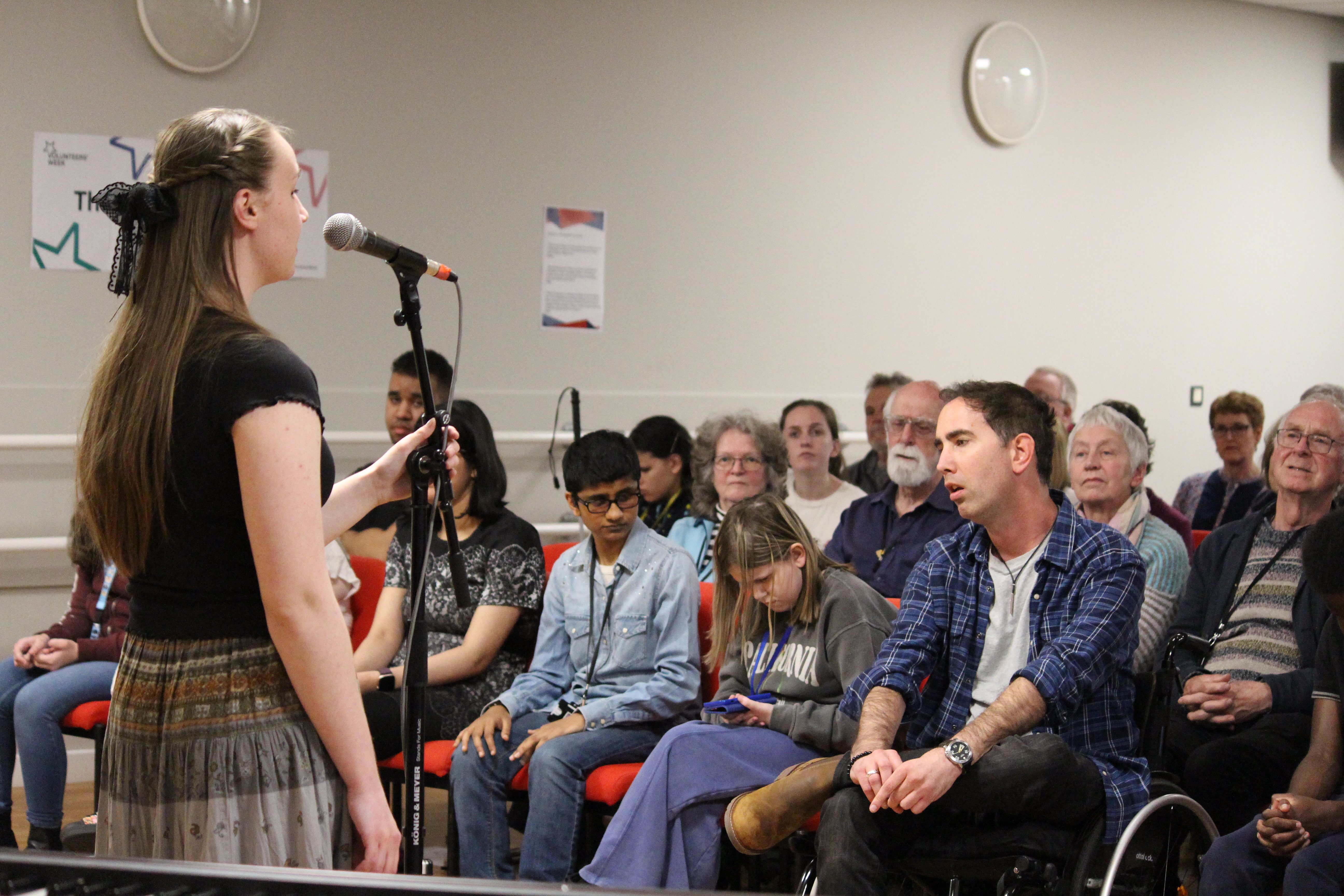 Lydia standing in front of the microphone with the audience in front of her