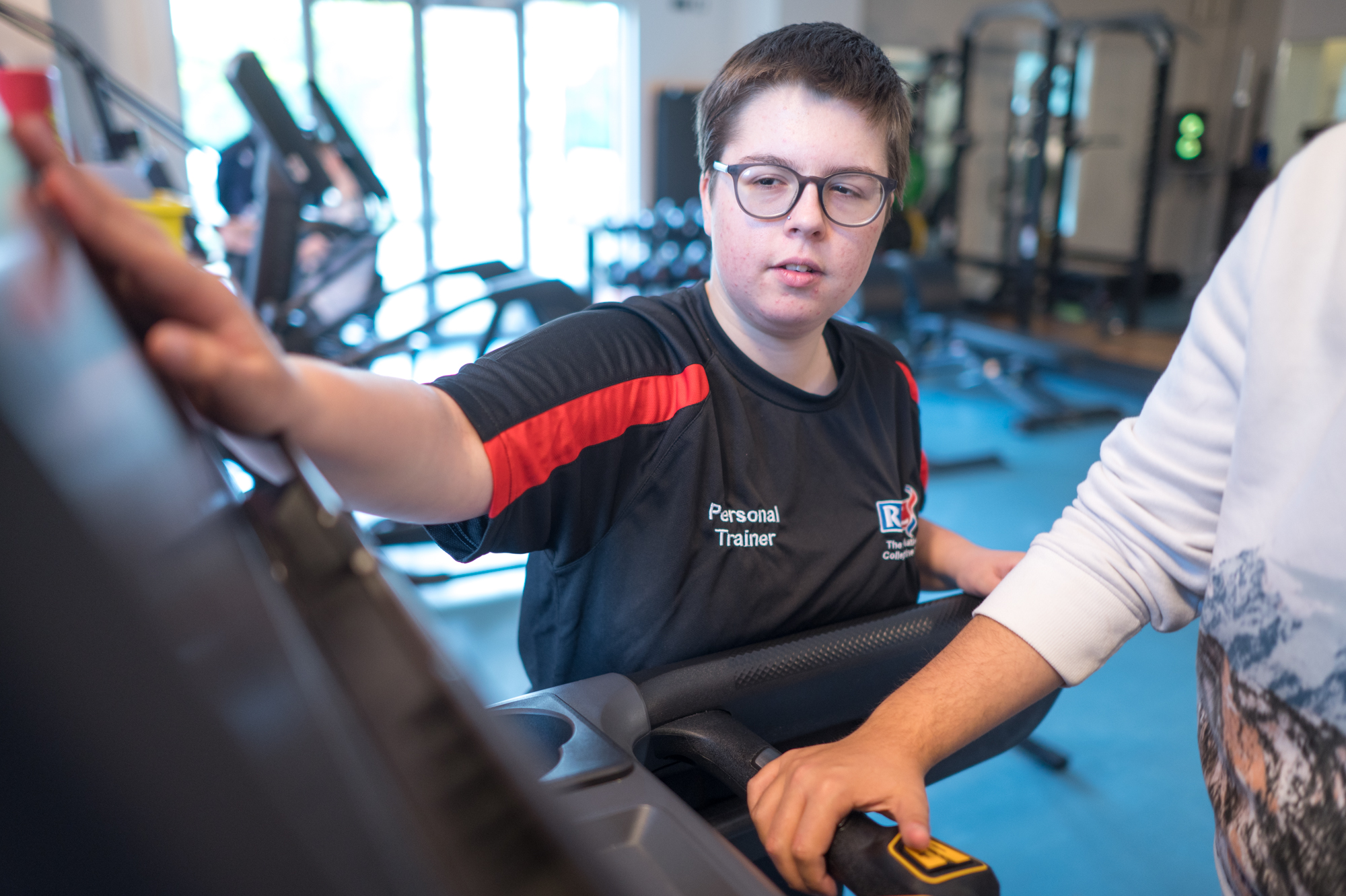 a personal trainer helps to set the treadmill buttons for a student