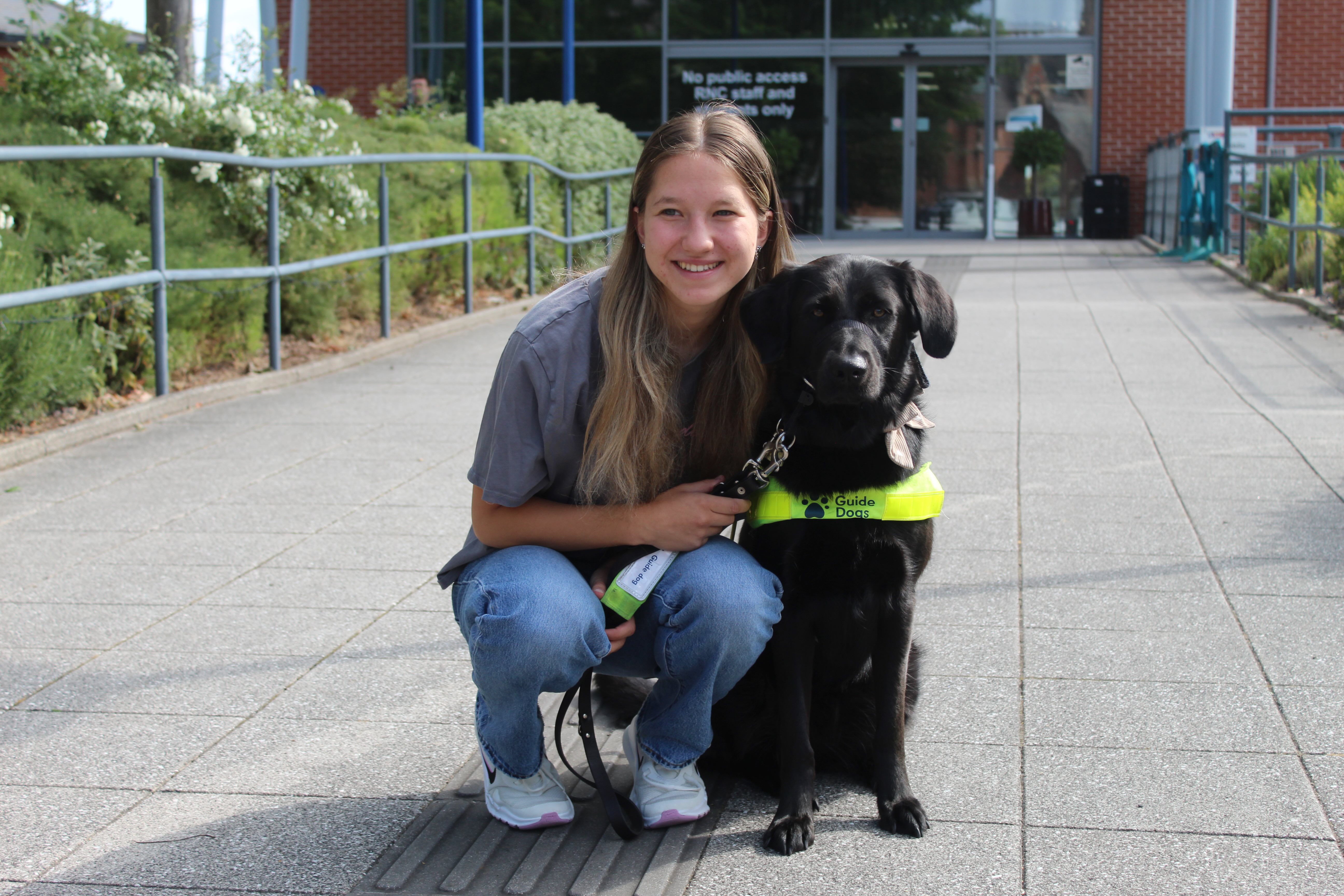 Lucja crouching down next to her guide dog Ulla in front of the entrance to the College